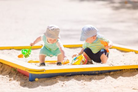 Two cute toddlers playing in a sandbox outside in the summer