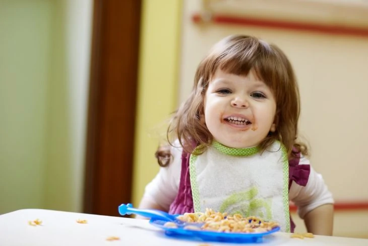 Little girl eating at table using a booster seat high chair