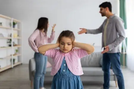 Little girl covering ears while her parents arguing at the back