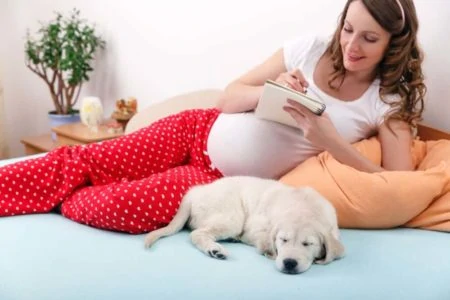 Pregnant woman writing on notebook in bed