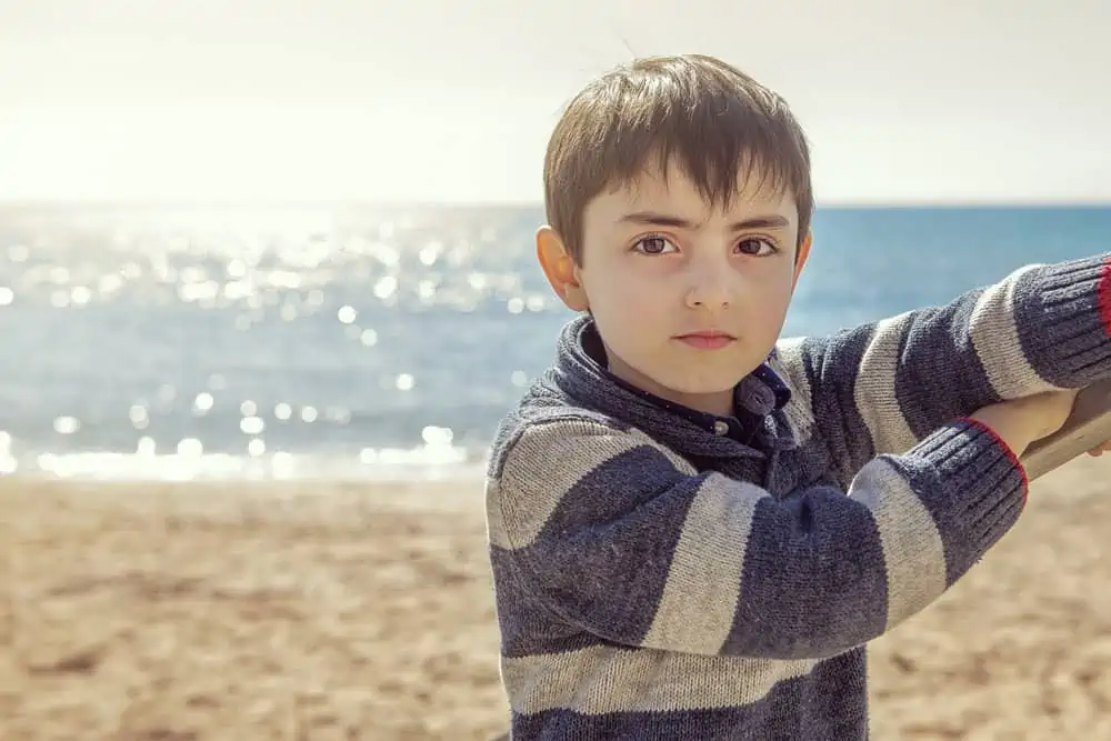 Adorable handsome boy looking at the camera near seashore on sunny day